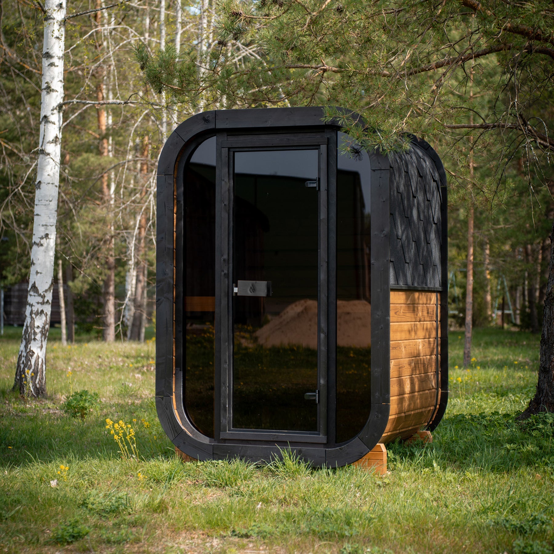 PlusLife Mini Traditional Sauna 2.0, a rounded-square outdoor cabin with a black rounded frame, full tinted-glass front, timber side cladding and black shingle roof